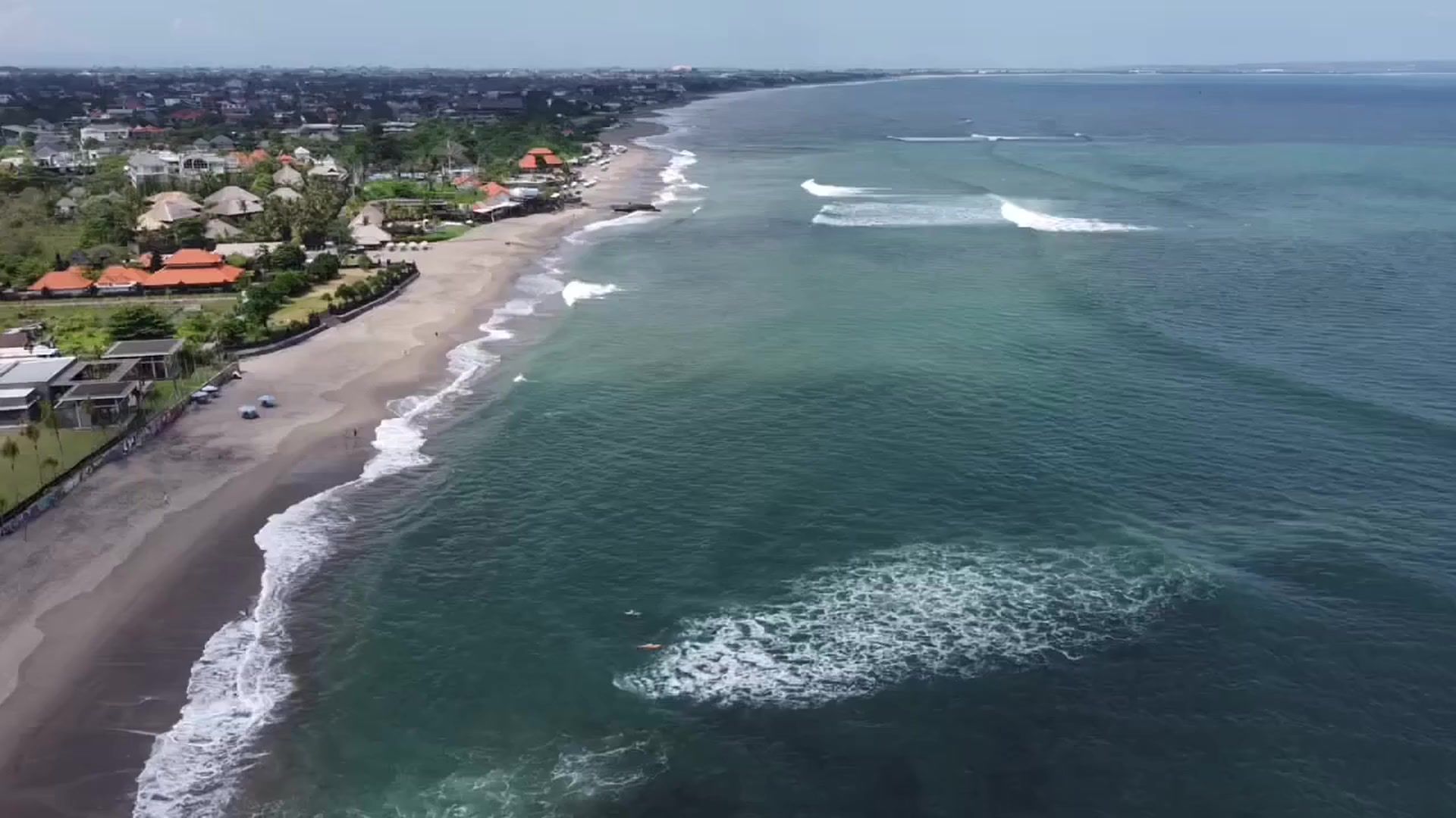 Aerial view of the Canggu coastline with surf breaking along the beach
