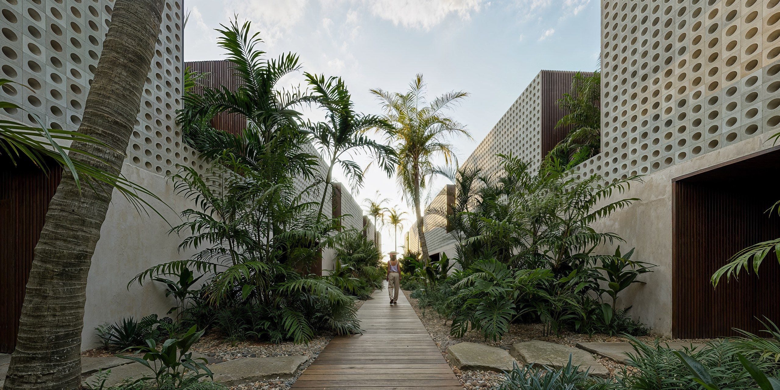 Walkway between the perforated facades of the villas, palms and tropical planting